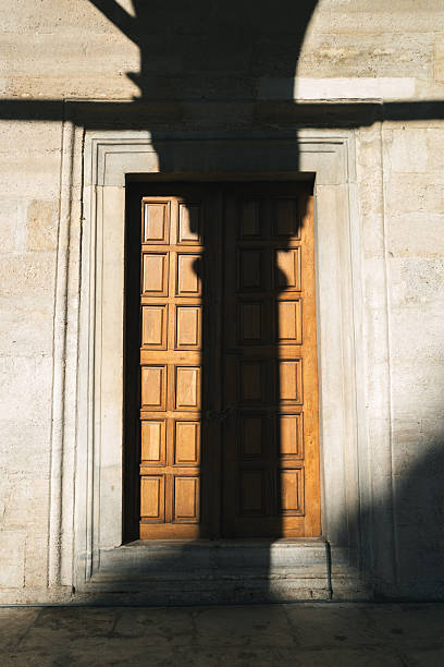 Ornate wooden door receiving afternoon sunlight and casting shadows on the stone wall