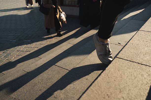 istock Person walking up stairs with long shadows 2253241227