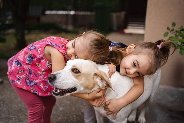 Two little sisters are hugging their dog in the backyard, showing love and affection