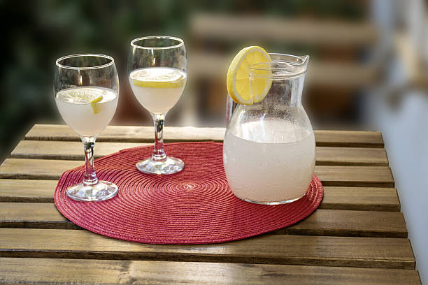 homemade lemonade served in glass pitcher with lemon slices and wine glasses on wooden garden table for refreshing summer drink on outdoor patio terrace