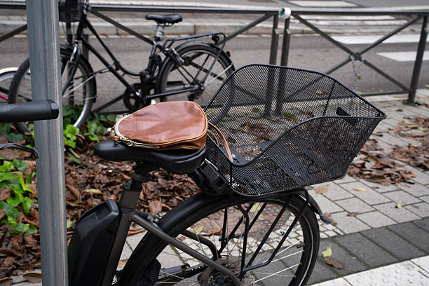 Leather bag with a kiss-lock clasp resting on a black bicycle seat outdoors. Everyday urban scene showing personal accessory casually placed on a bike.