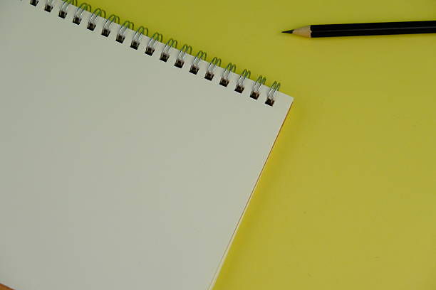 Open blank spiral notebook with black pencil on yellow background. Empty Space for your text. business and education concept
