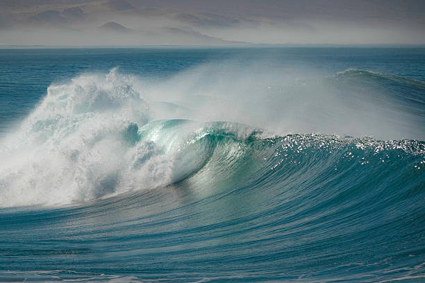 istock SILHOUETTE: Surfer paddling towards a big breaking wave with an offshore mist 2253254094