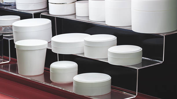 A row of different shaped and sized white empty plastic jars and bottles of various shapes with lids for liquids, cosmetics, pharmaceuticals or household chemicals stand in rows