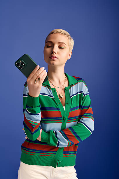 istock Captivating stylish woman examines her smartphone against a vibrant blue backdrop 2253260390