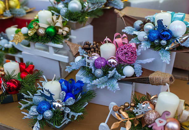 Decorative christmas candle arrangements with evergreen branches, ornaments, ribbons, and festive colors arranged on display stands. Seasonal decor concept for holiday celebration, home styling, winter mood, and gift inspiration.