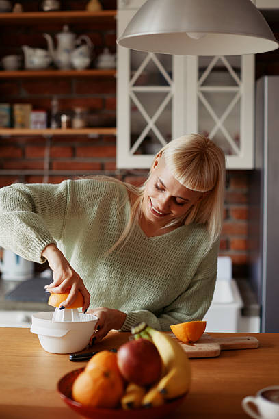 istock Young hipster woman enjoying her morning routine in a modern kitchen while making her morning orange drink 2253267222
