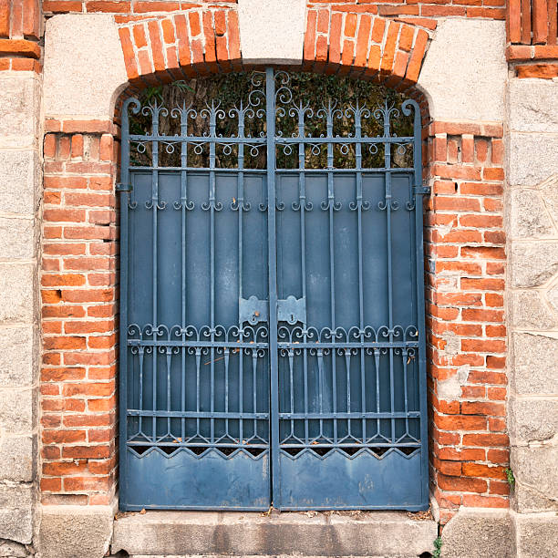 Closed blue wrought iron gate framed by a brick and stone archway, showing classic European architectural details and strong symmetry. Textured exterior background suitable for concepts such as security, entrance, heritage, protection, tradition, and urban architecture.