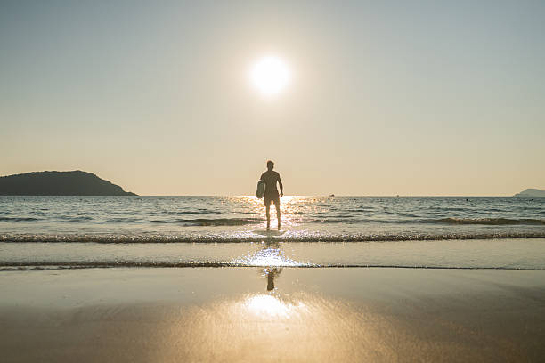 istock Young man entering ocean at sunset while holding surfboard expressing freedom and an adventurous beach lifestyle outdoor sports personal growth and inspirational summer lifestyle. 2253275109