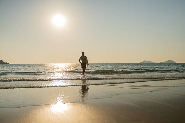 istock Young man entering ocean at sunset while holding surfboard expressing freedom and an adventurous beach lifestyle outdoor sports personal growth and inspirational summer lifestyle. 2253275110