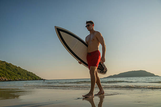istock Young man entering ocean at sunset while holding surfboard expressing freedom and an adventurous beach lifestyle outdoor sports personal growth and inspirational summer lifestyle. 2253275135