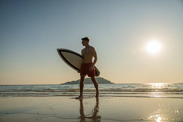istock Young man entering ocean at sunset while holding surfboard expressing freedom and an adventurous beach lifestyle outdoor sports personal growth and inspirational summer lifestyle. 2253275139