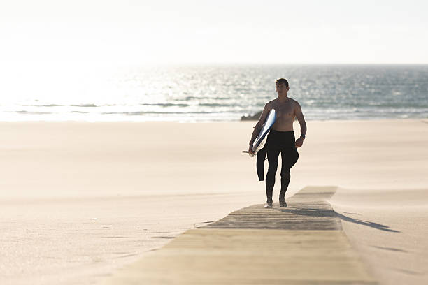 istock A man with naked torso walking on the path on the beach holding a surfboard 2253275592