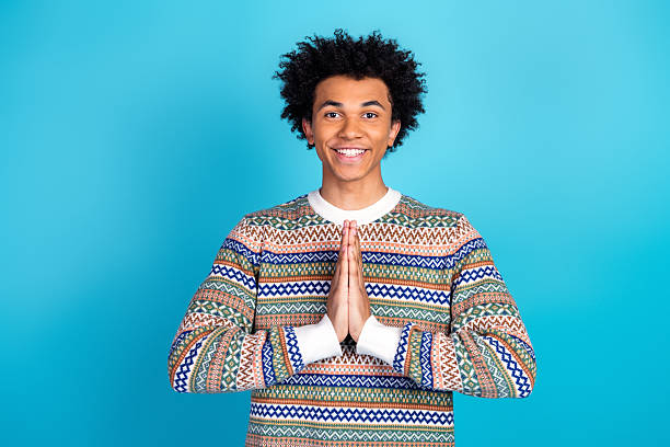 istock Young man in patterned sweater smiles with hands together against blue background 2253275656