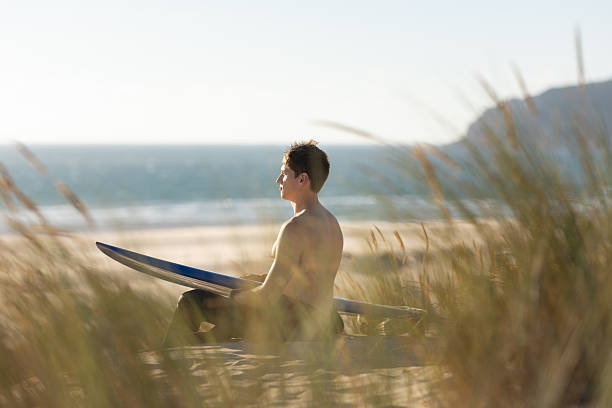 istock A man sitting on the beach holding a blue surfboard 2253276187