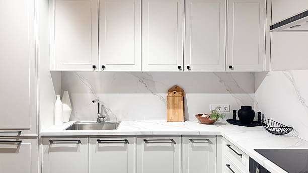 istock Bright modern kitchen interior with white cabinets, marble countertop, sink, black handles, stylish decor. 2253276979