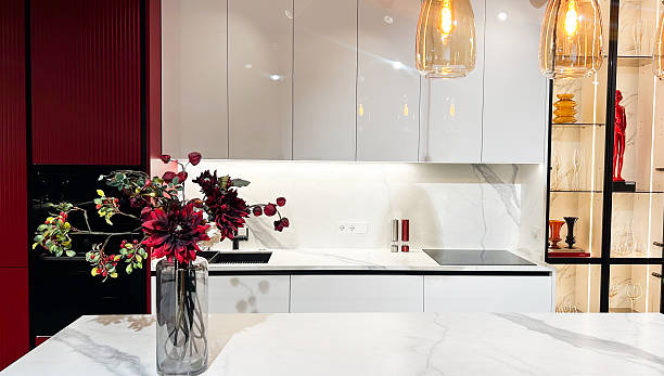 istock Modern kitchen interior with white marble counter, red wall, decorative flowers, pendant lights. 2253276993