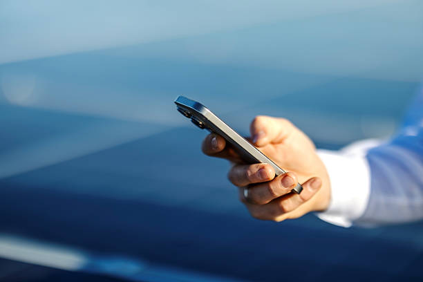 Person's hand holding a modern smartphone, actively engaging with mobile technology while standing outdoors, representing connectivity and digital communication