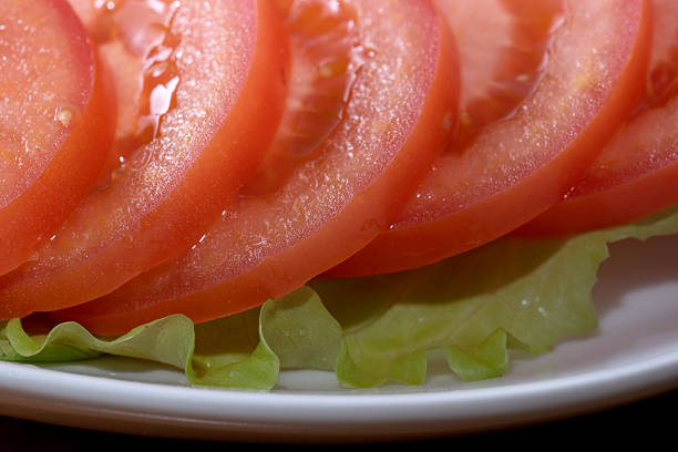 Bright red tomato slices overlap on fresh green lettuce, creating a vibrant plate.