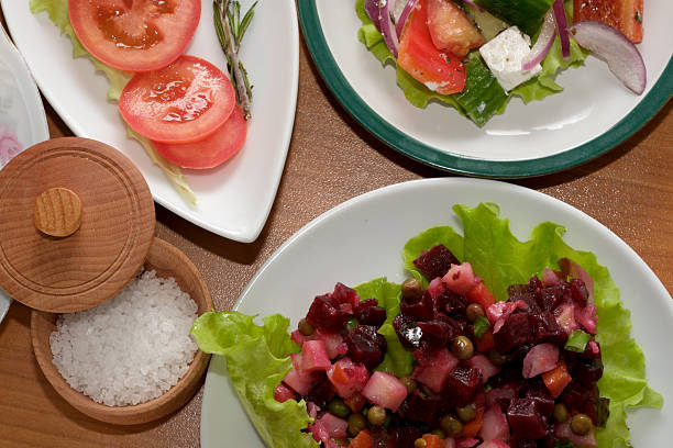 Delicious healthy meal featuring a fresh green salad topped with vibrant pomegranate seeds and shredded cheese, served alongside other prepared dishes on a dark wooden table