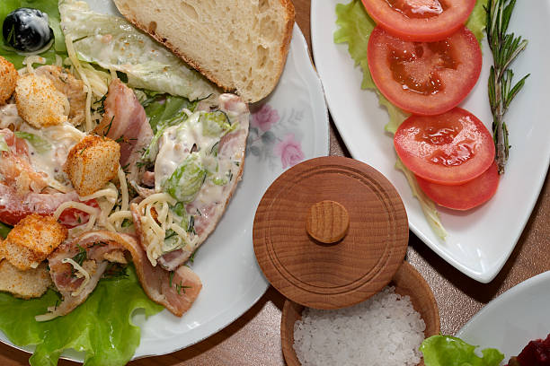 Tasty salad with greens, croutons, and a side of sliced tomatoes on wooden table.
