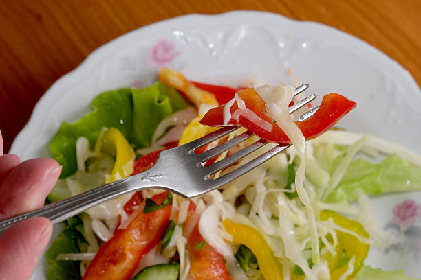 A hand holds a fork with fresh vegetables, highlighting a healthy salad.