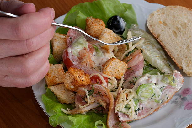 A hand picks up a fork to enjoy a fresh salad with vibrant greens and toppings.