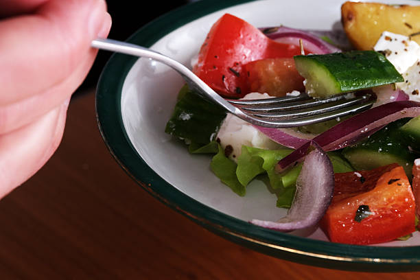 Point of view of man's hand holding fork to eat a salad of vegetables and fruit.vegetarian and vegan diet for nutrition and healthy lifestyle.organic tomato and home garden veggies.