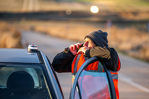 Driver placing a V16 warning or emergency beacon with a broken-down vehicle on the road, calling for a tow truck, using the emergency signal and warning triangle. This beacon will be mandatory in Spain by 2026. Tordesillas, Valladolid, Castile and León, Spain, Europe - December 21, 2025.