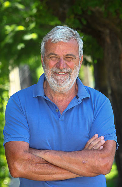 Portrait of a cheerful senior Latino man smiling outdoors with lush greenery in the background.
