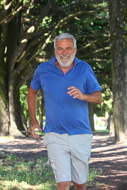 Cheerful senior Latino man jogging outdoors with lush greenery in the background.