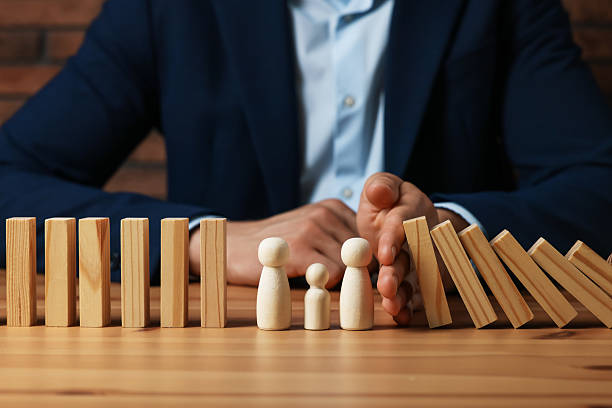 istock Risk. Man protecting human figures from domino effect at wooden desk, closeup 2253284101