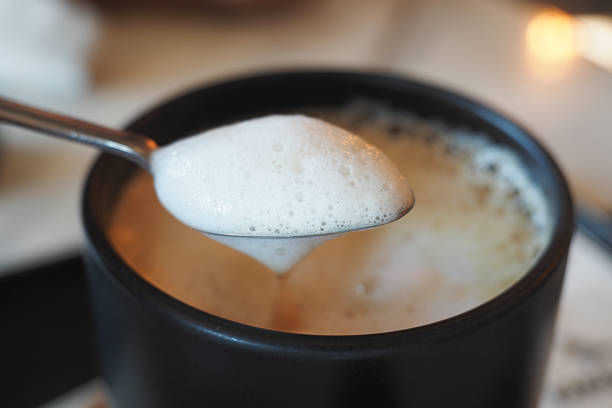 A close view of coffee foam resting on a spoon above a black mug.