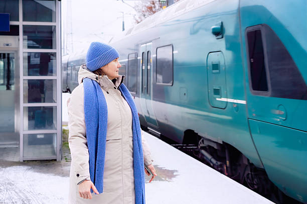 A middle-aged woman stands on the snowy platform, observing the arriving winter train with calm anticipation, expressing the concept of active ageing and purposeful seasonal travel.