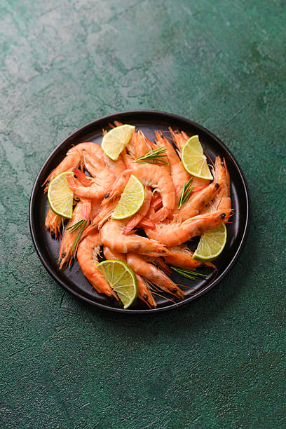 istock Shrimp and lime in black bowl on green rustic surface for seafood freshness or summer menu concept 2253293536