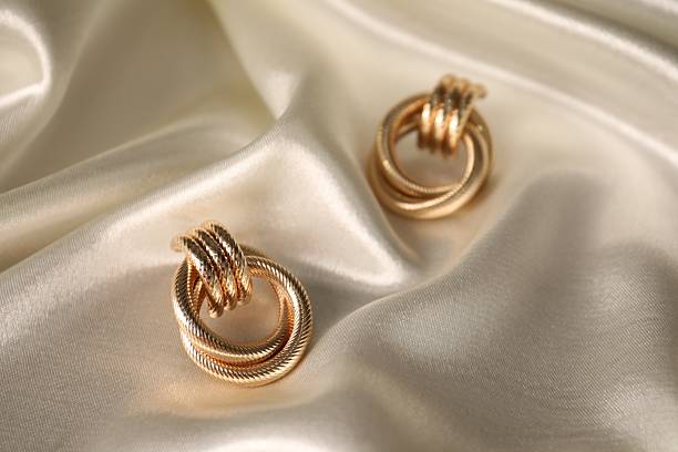 Stylish gold earrings on light silk cloth, closeup