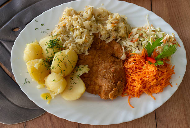 A homestyle plate with crispy breaded cutlet, boiled potatoes with dill, braised cabbage, and fresh carrot and cabbage salads. Comfort food concept, balanced meal, rustic table setting, and everyday cooking.