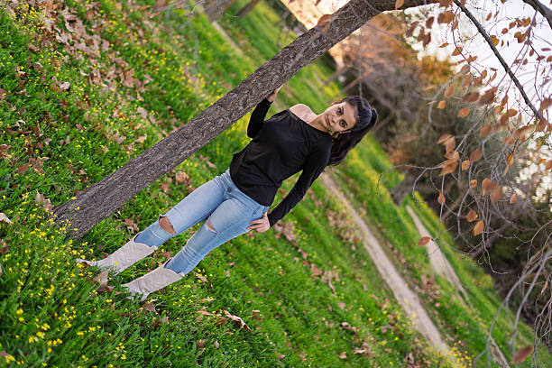 Young woman leaning against tree in a meadow at sunset
