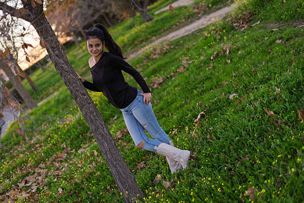 Young woman with ponytail leaning against a tree in a park during sunset