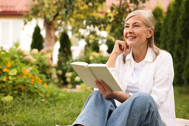 istock Senior woman reading book on green grass outdoors, space for text 2253300856