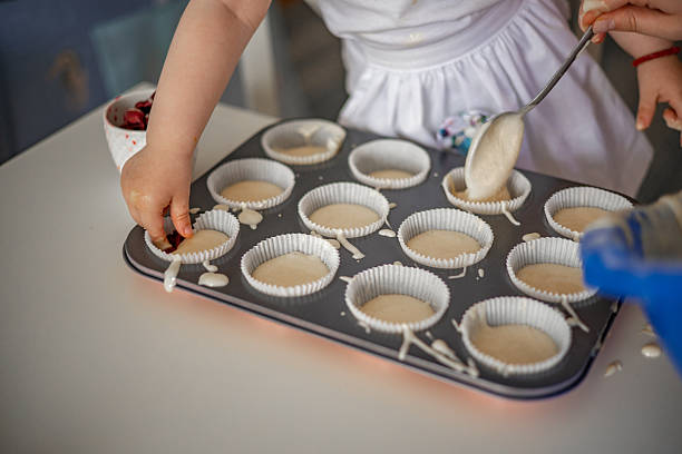 A playful baking moment as a mother and daughter pour batter into cupcake liners together, turning cooking into a fun family activity