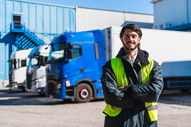 istock Truck driver in reflective jacket standing by semi-trucks 2253302640