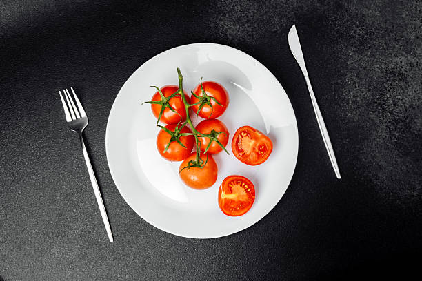 istock Fresh cherry tomatoes arranged on a white plate with cutlery on a dark surface 2253302696