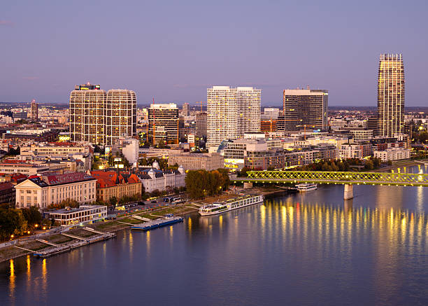 Bratislava, Slovakia - October 18, 2025: Aerial view of a Bratislava city skyline at dusk, featuring modern skyscrapers, Danube river, and illuminated buildings reflecting on the water