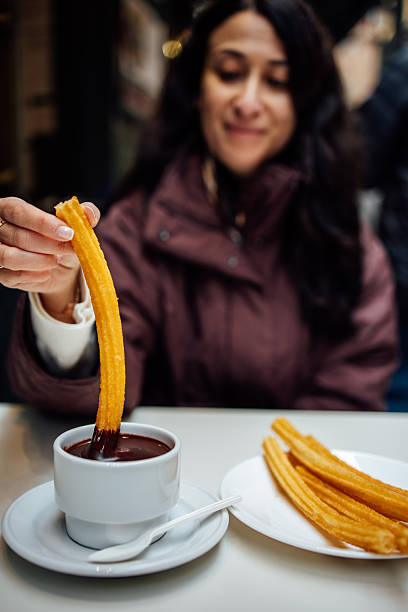 Woman dipping traditional Spanish churros into hot chocolate sauce at a cafe.