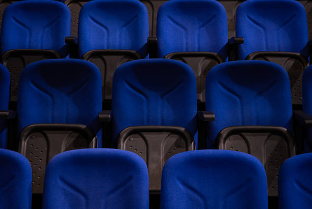 Rows of vibrant blue suede stadium seats with dark gray armrests and backs are seen from an elevated perspective, creating a repetitive pattern and dynamic leading lines within an empty theater