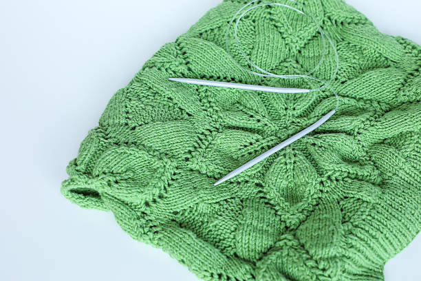 Circular knitting needles rest on a hand-knitted green sweater featuring a distinctive cable pattern, highlighting traditional craftsmanship and the art of handmade knitting. Perfect for DIY, crafting, hobby, and creative projects.