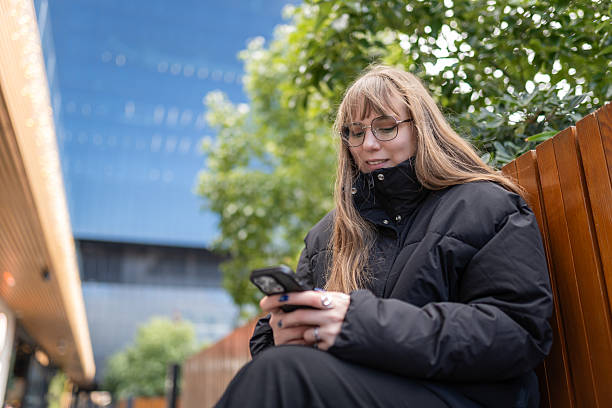 istock Young woman sitting outdoors using smartphone for remote communication and digital connection 2253310904