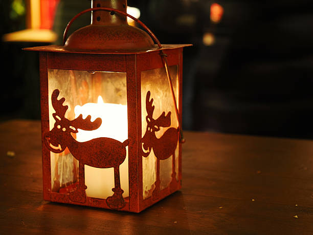 Decorative Christmas lantern with reindeer silhouettes illuminated by candlelight on wooden surface