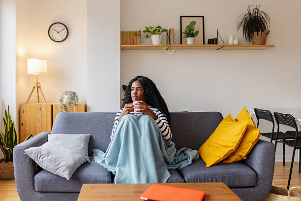 istock Young black woman drinking hot coffee while sitting on sofa at home in winter 2253311991